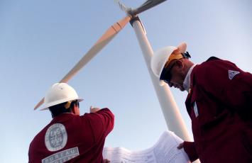 Imagem de dois colaboradores uniformizados do Bureau Veritas analisando uma turbina de energia eólica ao fundo