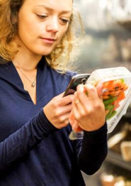 Imagem de uma mulher olhando para seu celular e segurando uma embalagem de alimentos