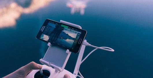 Imagem de uma pessoa olhando para um celular que exibe a vista de um drone