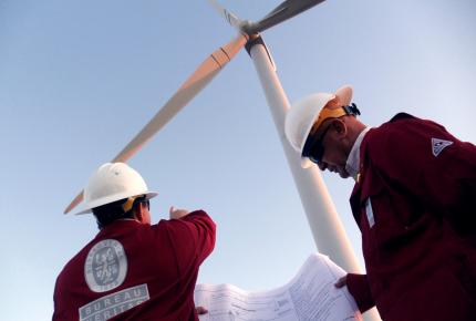 Imagem de dois colaboradores uniformizados do Bureau Veritas analisando uma turbina de energia eólica ao fundo